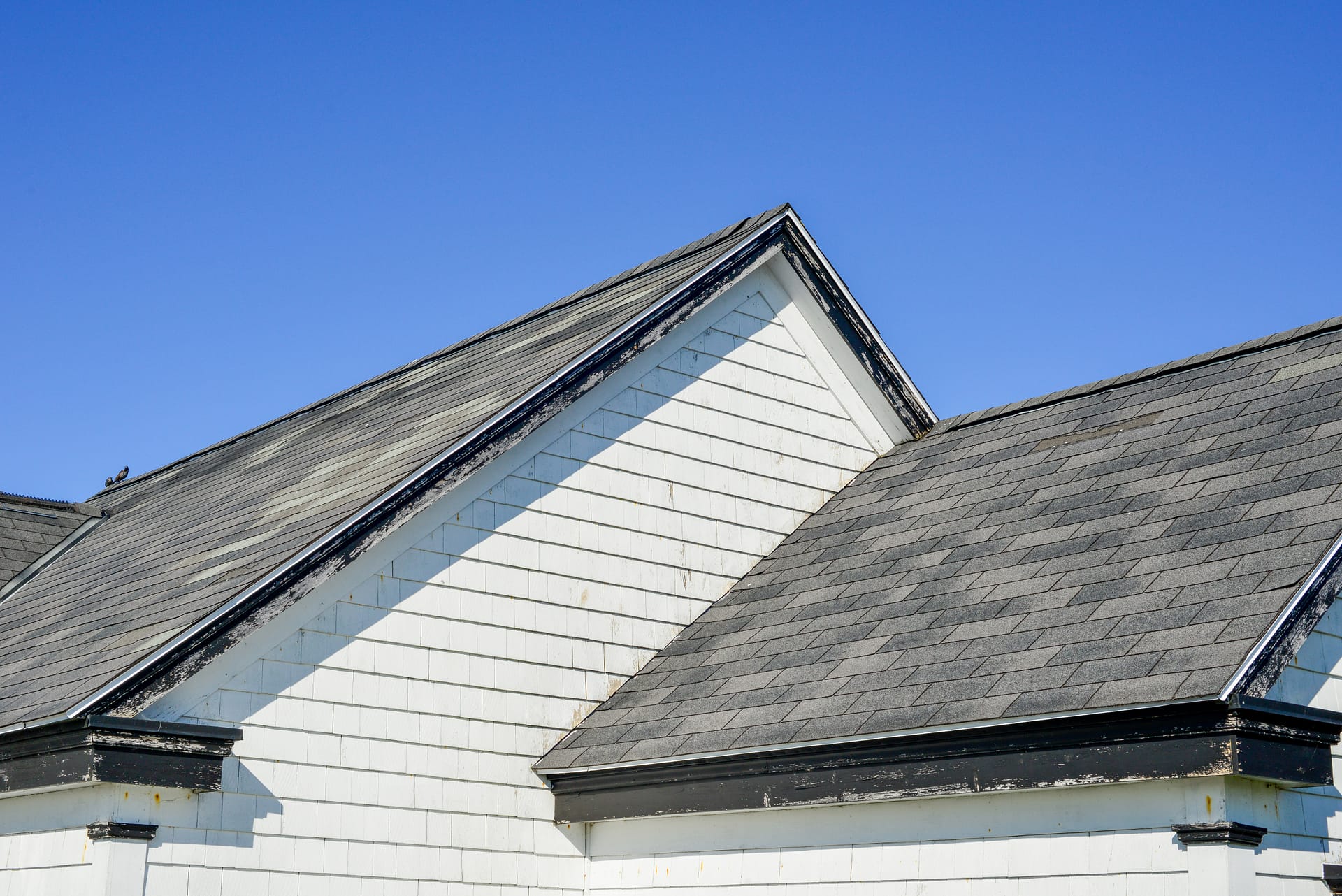 Multiple peaked and layered roofs on a white vintage wooden house. The eave is painted black. The shingles on the roof are grey in color. The old building has wood horizontal clapboard siding. Multiple peaked and layered roofs on a white vintage wooden house. The eave is painted black. The shingles on the roof are grey in color. The old building has wood horizontal clapboard siding.