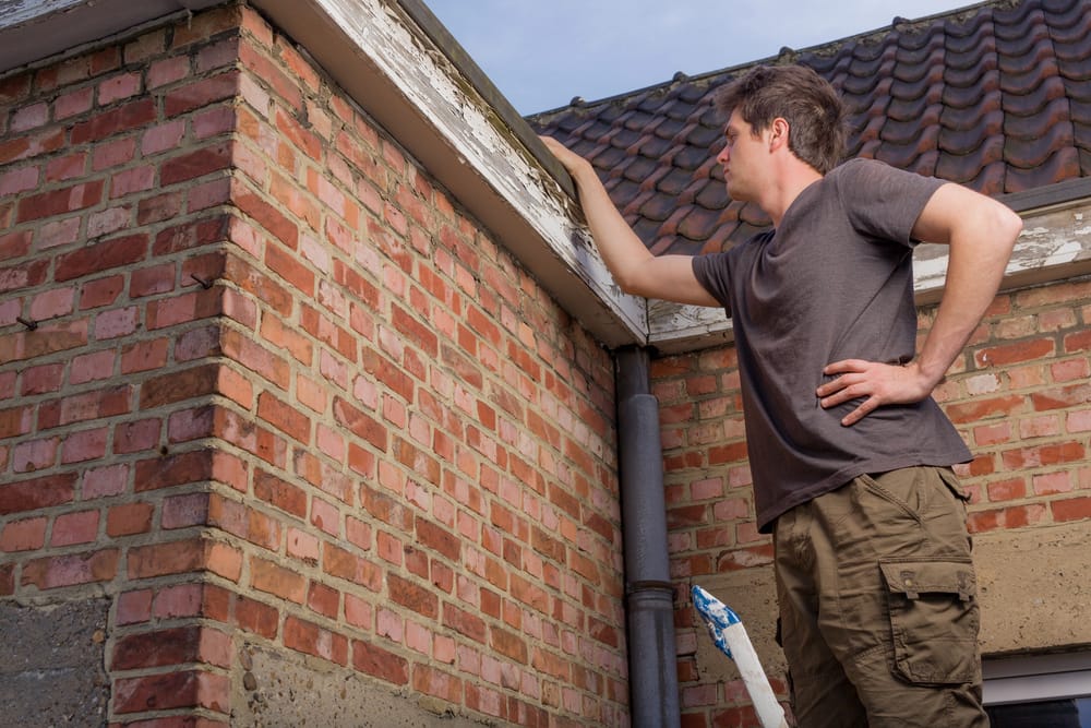 Young man inspecting the roof of an old house considering a DIY roofing project.