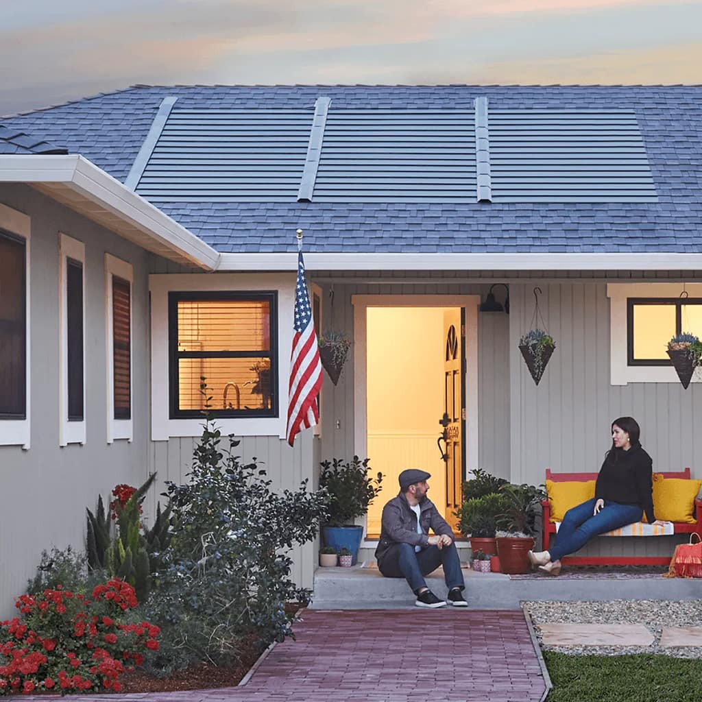 Charming home exterior featuring innovative solar shingles on the roof, surrounded by a vibrant garden and inviting porch, perfect for enjoying the evening light.