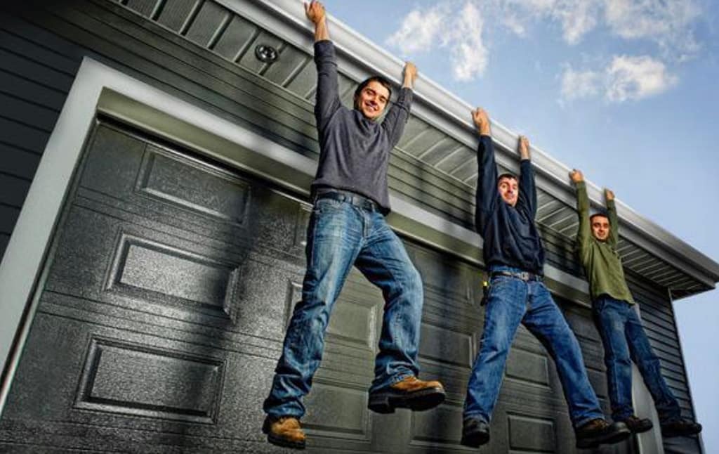 Three men hanging from a home gutter to demonstrate the strength and durability of Alu-Rex gutter guards above a garage.