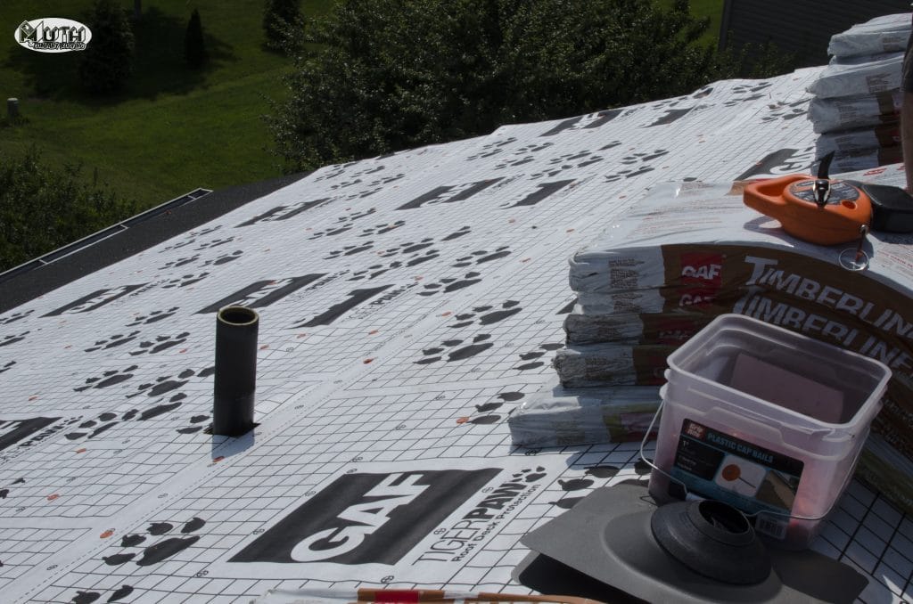 A view of a roof with GAF Timberline shingles and installation materials, showcasing workers installing a new roof.