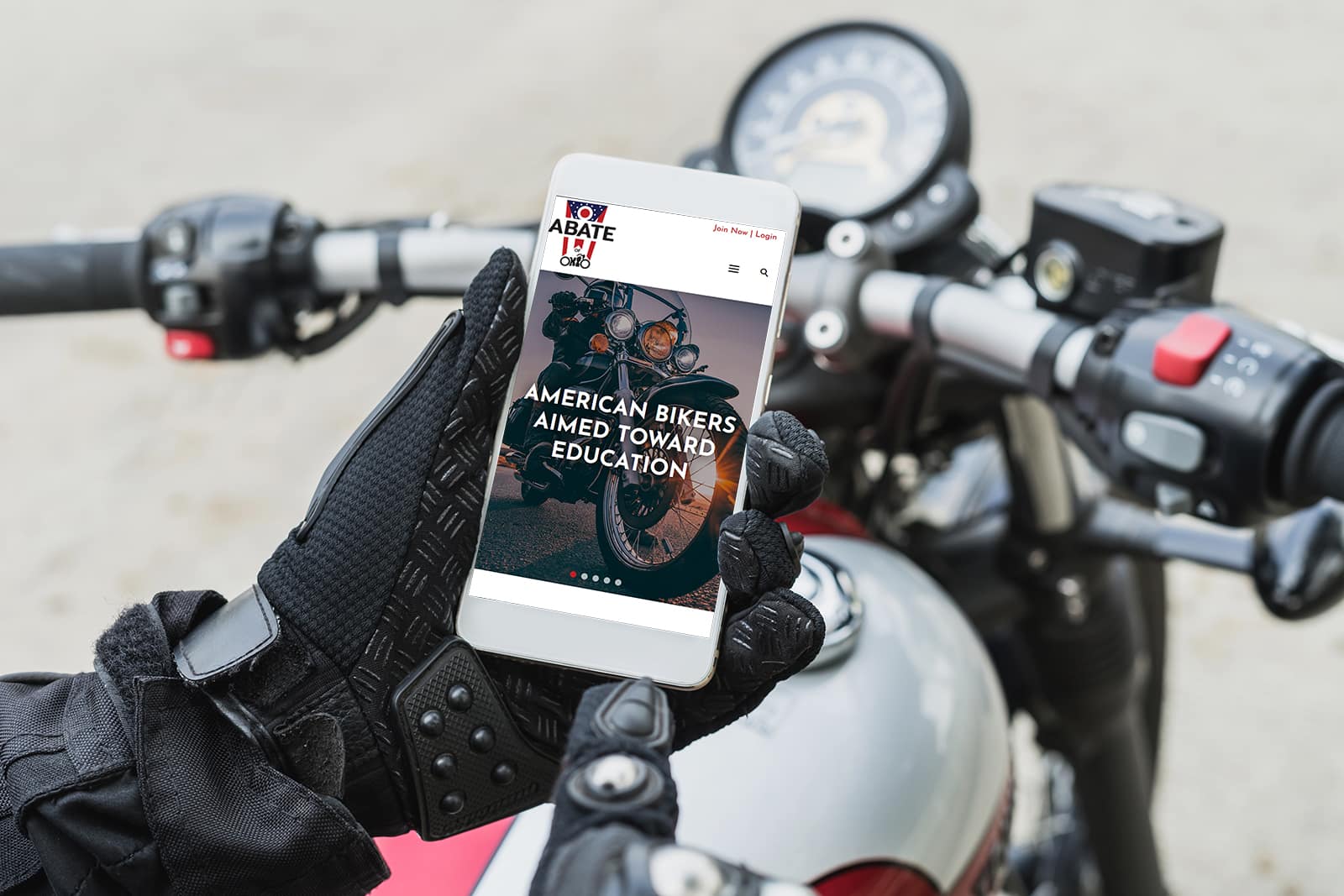 ABATE website homepage on mobile phone held by motorcyclist with bike in the background