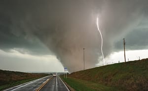 Ohio Tornado Season storm with large tornado touching down near a rural highway as lightning strikes in the distance.