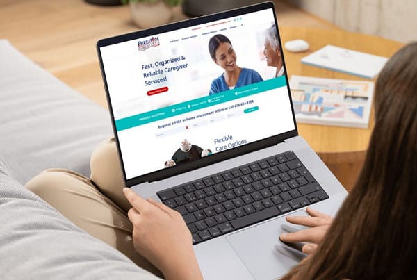 Freedom Caregivers homepage pulled up on laptop held by a woman on a couch