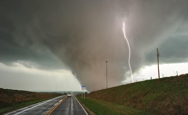 Ohio Tornado Season storm with large tornado touching down near a rural highway as lightning strikes in the distance.