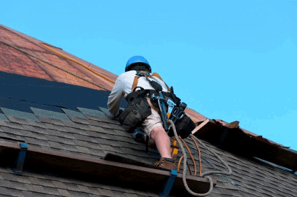 The image shows a roofer wearing a safety harness system for fall protection while working on a roof. The roofer is well withing safety compliance.